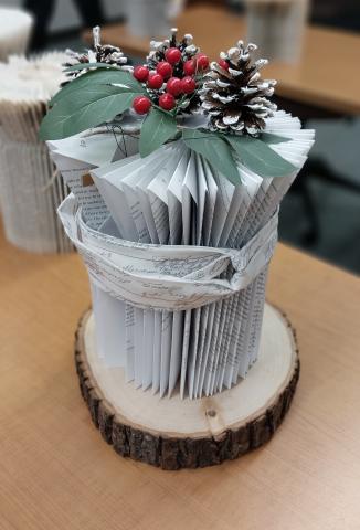 Folded book pages into a platform, with decorative Holi berry on top. The platform is sitting on a wooden charger. 