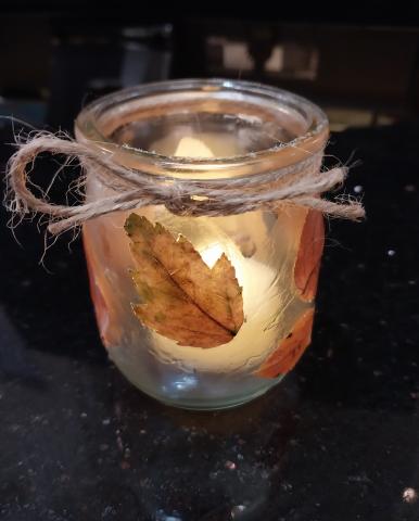 Small mason jar with electric tea light inside that has twine wrapped around the rim and leaves. 