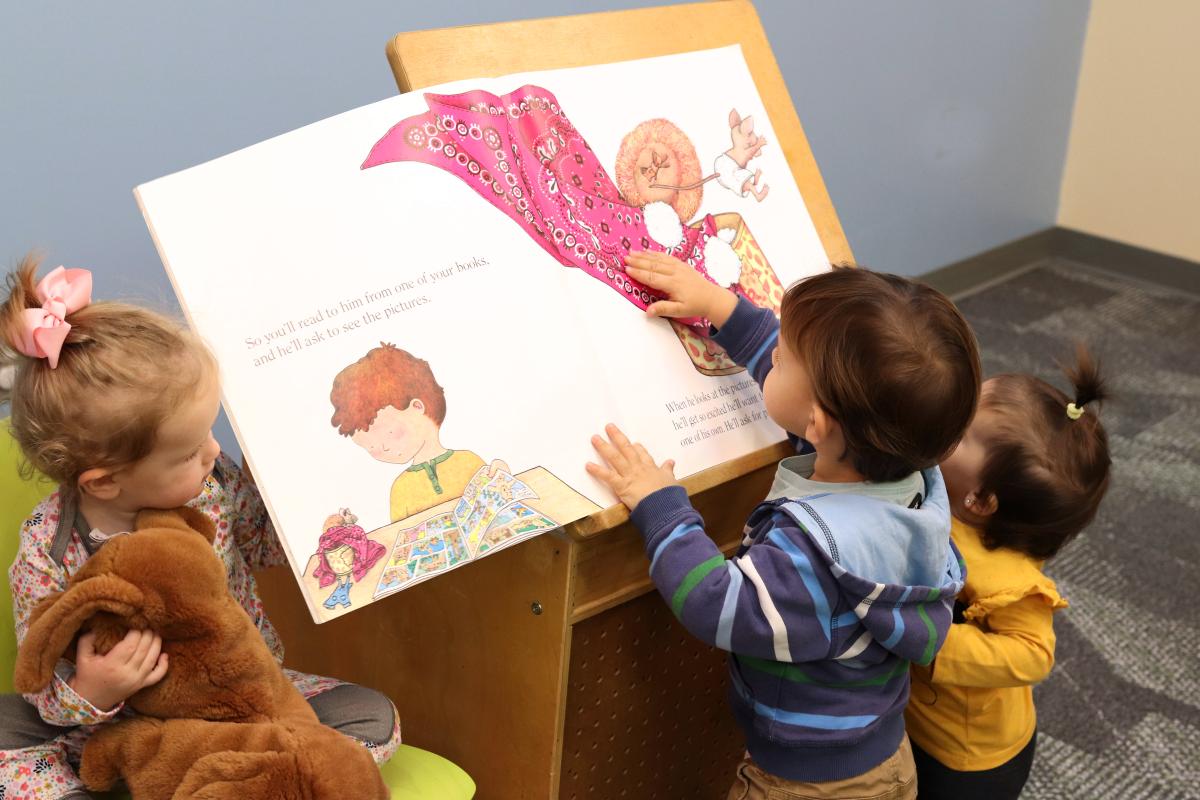 Image of three toddlers looking at a story book